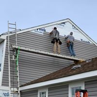 Two workers installing new tan colored vinyl siding.